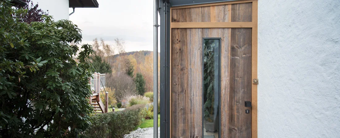 Eingang mit rustikaler Holztür und Blick in einen begrünten Garten